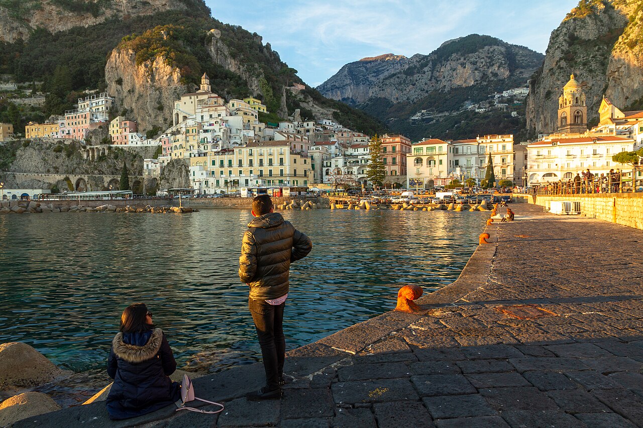 Die Stadt Amalfi im goldenen Abendlicht, vom Hafenpier aus gesehen, mit Klippen und bunten Häusern