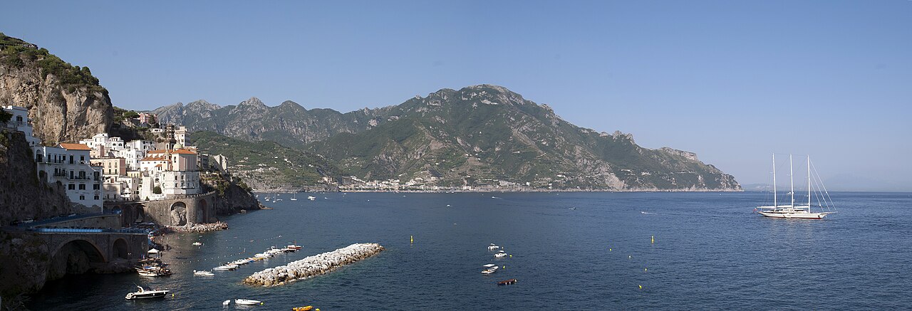 Weites Panorama der Amalfiküste mit dem Ort Atrani an der Klippe, den Bergen und dem tiefblauen Meer