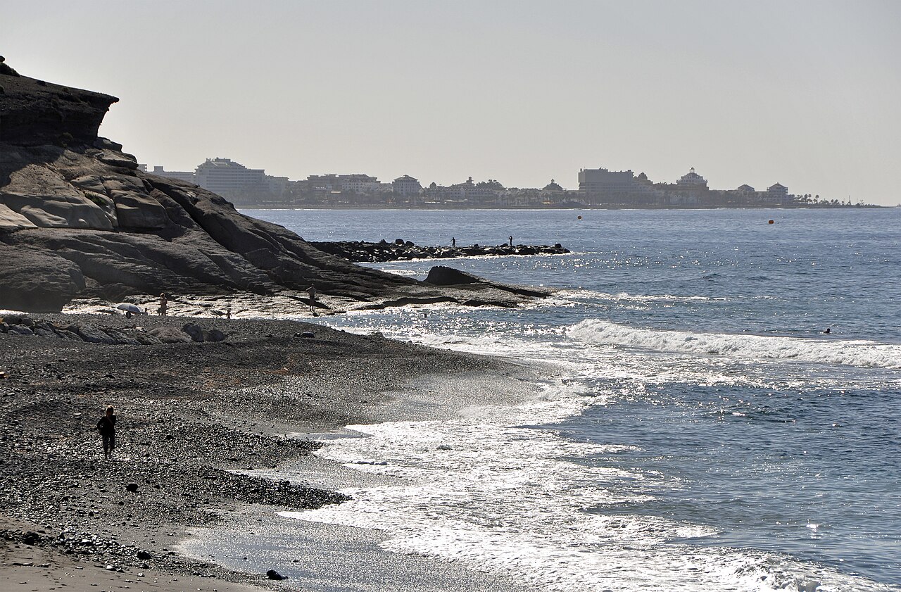 Strand an der Costa Adeje auf Teneriffa mit der Hotelzeile im sonnigen Gegenlicht