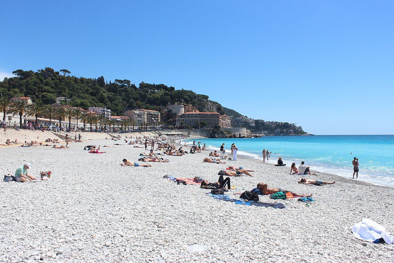 Die flache Promenade des Anglais in Nizza mit Kiesstrand, Palmen und der Hotelzeile dahinter